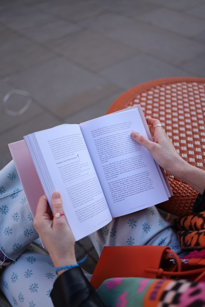 Close-up of hands holding an open book while seated outdoors.